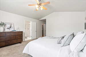 Carpeted bedroom featuring ensuite bath, lofted ceiling, a ceiling fan, and baseboards
