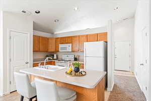 Kitchen featuring a sink, brown cabinetry, white appliances, light countertops, and visible vents
