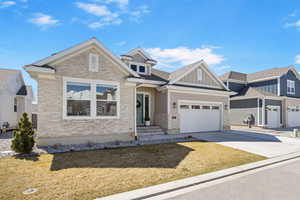 View of front of home with driveway, stone siding, a garage, and board and batten siding
