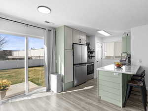 Kitchen featuring a breakfast bar area, stainless steel appliances, light wood finished floors, visible vents, and a peninsula