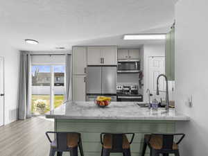 Kitchen featuring a breakfast bar area, light wood-type flooring, a textured ceiling, a peninsula, and appliances with stainless steel finishes
