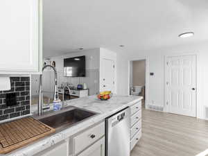 Kitchen with light stone countertops, dishwasher, visible vents, white cabinets, and light wood-style floors
