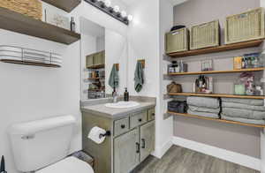 Bathroom featuring toilet, vanity, baseboards, and wood finished floors