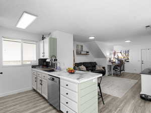 Kitchen with stainless steel dishwasher, open floor plan, light wood finished floors, and a kitchen bar