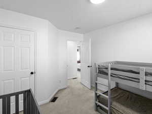 Bedroom with baseboards, a textured ceiling, visible vents, and light carpet