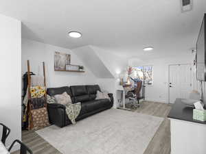 Living area featuring baseboards, visible vents, light wood-style floors, and a textured ceiling