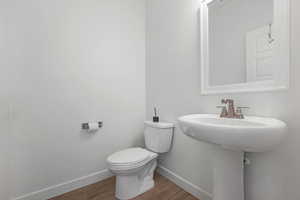 Half bathroom with baseboards, wood finished floors, and toilet