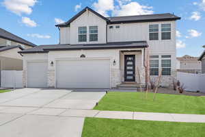 View of front of home featuring a front yard, stone siding, concrete driveway, fence, and board and batten siding
