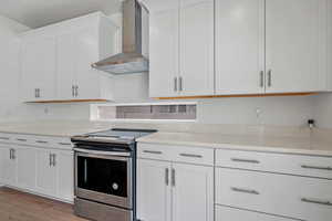 Kitchen featuring stainless steel range with electric stovetop, white cabinets, light countertops, light wood finished floors, and wall chimney exhaust hood
