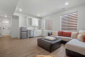 Living room with wet bar, light wood finished floors, baseboards, visible vents, and recessed lighting