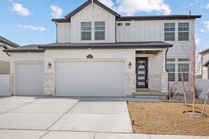 View of front of property with stone siding, board and batten siding, concrete driveway, and a garage