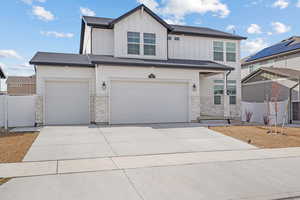 View of front of house with stone siding, driveway, fence, and board and batten siding