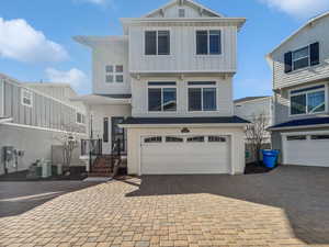 View of front facade featuring board and batten siding, decorative driveway, a garage, and central air condition unit