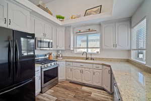 Kitchen with a sink, white cabinetry, light wood-type flooring, and appliances with stainless steel finishes
