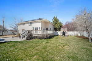 Rear view of property with a fenced backyard, a deck, solar panels, a lawn, and a patio area