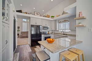 Kitchen featuring a kitchen breakfast bar, stainless steel appliances, a sink, light stone counters, and a peninsula