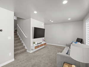 Carpeted living area with baseboards, recessed lighting, and stairway