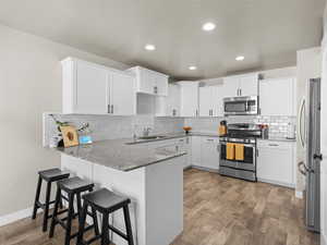 Kitchen with a peninsula, appliances with stainless steel finishes, a sink, light wood-type flooring, and light stone counters