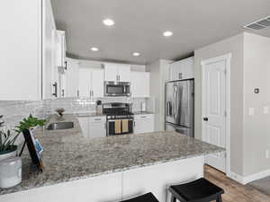Kitchen with tasteful backsplash, stainless steel appliances, light stone countertops, a sink, and a peninsula