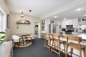 Kitchen with white cabinetry, a kitchen bar, open shelves, stainless steel appliances, and backsplash