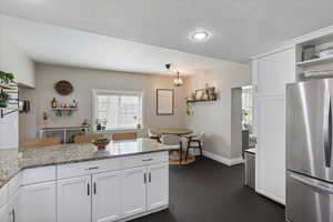 Kitchen with white cabinetry, open shelves, light stone countertops, and freestanding refrigerator