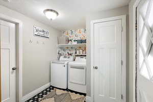 Clothes washing area with baseboards, washer and dryer, laundry area, and a textured ceiling