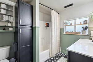 Full bathroom with a textured ceiling, visible vents, toilet, vanity, and shower / tub combo