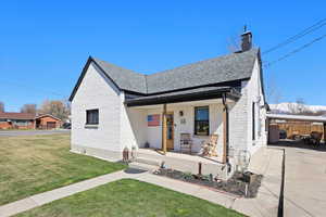 View of front of property featuring a front yard, roof with shingles, a chimney, brick siding, and a porch
