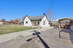 View of front of property featuring a front lawn, a detached carport, a chimney, and aphalt driveway
