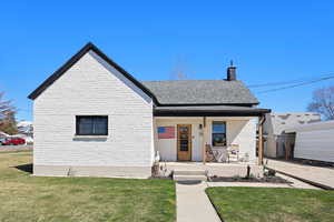 View of front of home with covered porch, a chimney, a front lawn, and roof with shingles