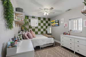 Bedroom with a textured ceiling, visible vents, baseboards, wood finished floors, and an accent wall