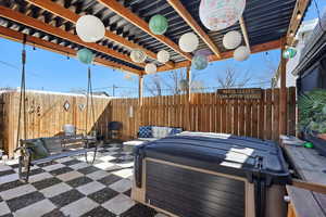 View of patio with a hot tub and fence