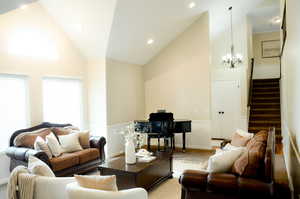 Living room with a chandelier, stairs, high vaulted ceiling, and baseboards