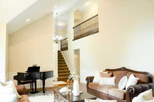 Living room with baseboards, a high ceiling, a chandelier, stairs, and carpet flooring