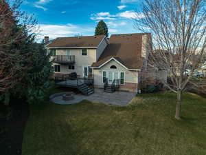 Back of property featuring a patio, a balcony, a chimney, entry steps, and a lawn