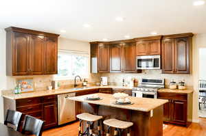 Kitchen with light wood-type flooring, appliances with stainless steel finishes, decorative backsplash, and a sink