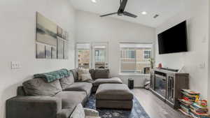 Living room featuring healthy amount of natural light, wood finished floors, a ceiling fan, lofted ceiling, and a glass covered fireplace