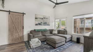 Living room featuring a barn door, wood finished floors, a ceiling fan, baseboards, and a towering ceiling
