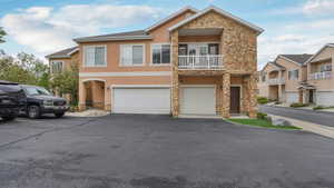 View of front of property with stone siding, a garage, stucco siding, driveway, and a balcony
