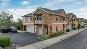 View of side of property with stone siding, stucco siding, a garage, a residential view, and a balcony