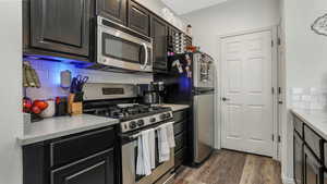 Kitchen featuring stainless steel appliances, decorative backsplash, and dark wood-style flooring