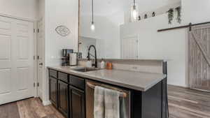 Kitchen with dishwasher, a sink, a barn door, light wood finished floors, and light stone countertops