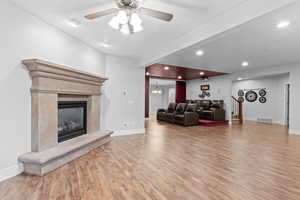 Living room with wood finished floors, ceiling fan, baseboards, a fireplace, and recessed lighting