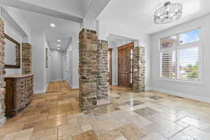 Wine area with stone tile floors, baseboards, a chandelier, recessed lighting, and ornate columns