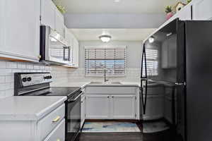 Kitchen featuring light countertops, tasteful backsplash, white cabinetry, a sink, and black appliances