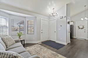 Foyer entrance featuring dark wood-style flooring, plenty of natural light, lofted ceiling, and a chandelier