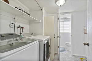 Washroom with washing machine and dryer, baseboards, laundry area, and a textured ceiling