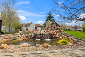 Community sign with a small pond, a lawn, a residential view, and fence