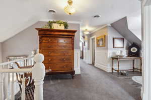 Living area featuring lofted ceiling, carpet, visible vents, and a wainscoted wall