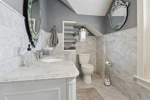 Bathroom with toilet, tile walls, a sink, and wainscoting